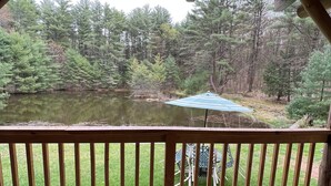 A wooden deck with a railing overlooking a pond surrounded by trees.