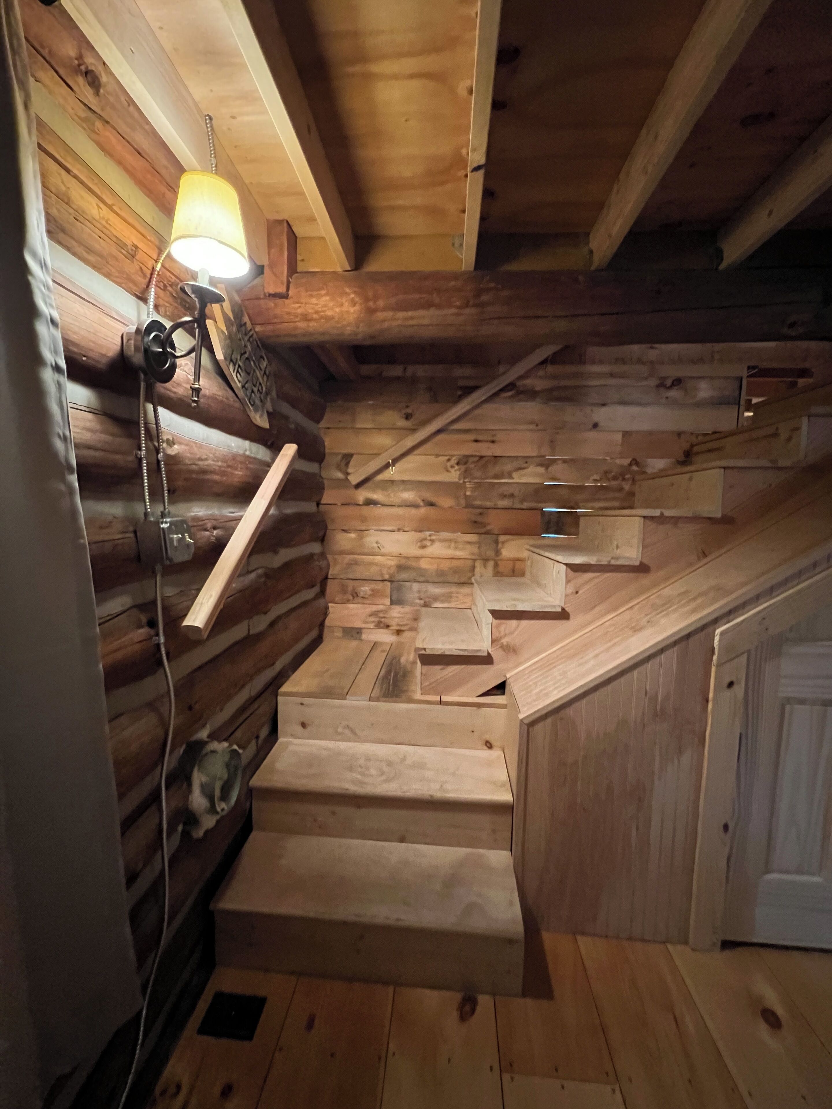 Un escalier en bois, doté d’une rampe et d’un luminaire fixé au mur.