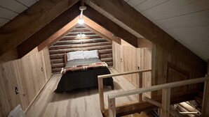 A cozy attic bedroom with a sloped ceiling, a wooden bed, and a small staircase.