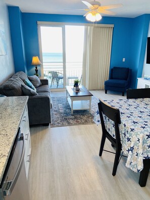 A room with a sofa, a dining table, a chair, a ceiling fan, and a view of the ocean through a sliding door. - Lux OceanWalk Condo 2BR 2BA 3Bal OceanFront uni501 (Daytona Beach)