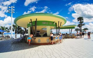 A beachside bar with a green and yellow color scheme, located on a paved area with palm trees and beach chairs. - Lux OceanWalk Condo 2BR 2BA 3Bal OceanFront uni501 (Daytona Beach)