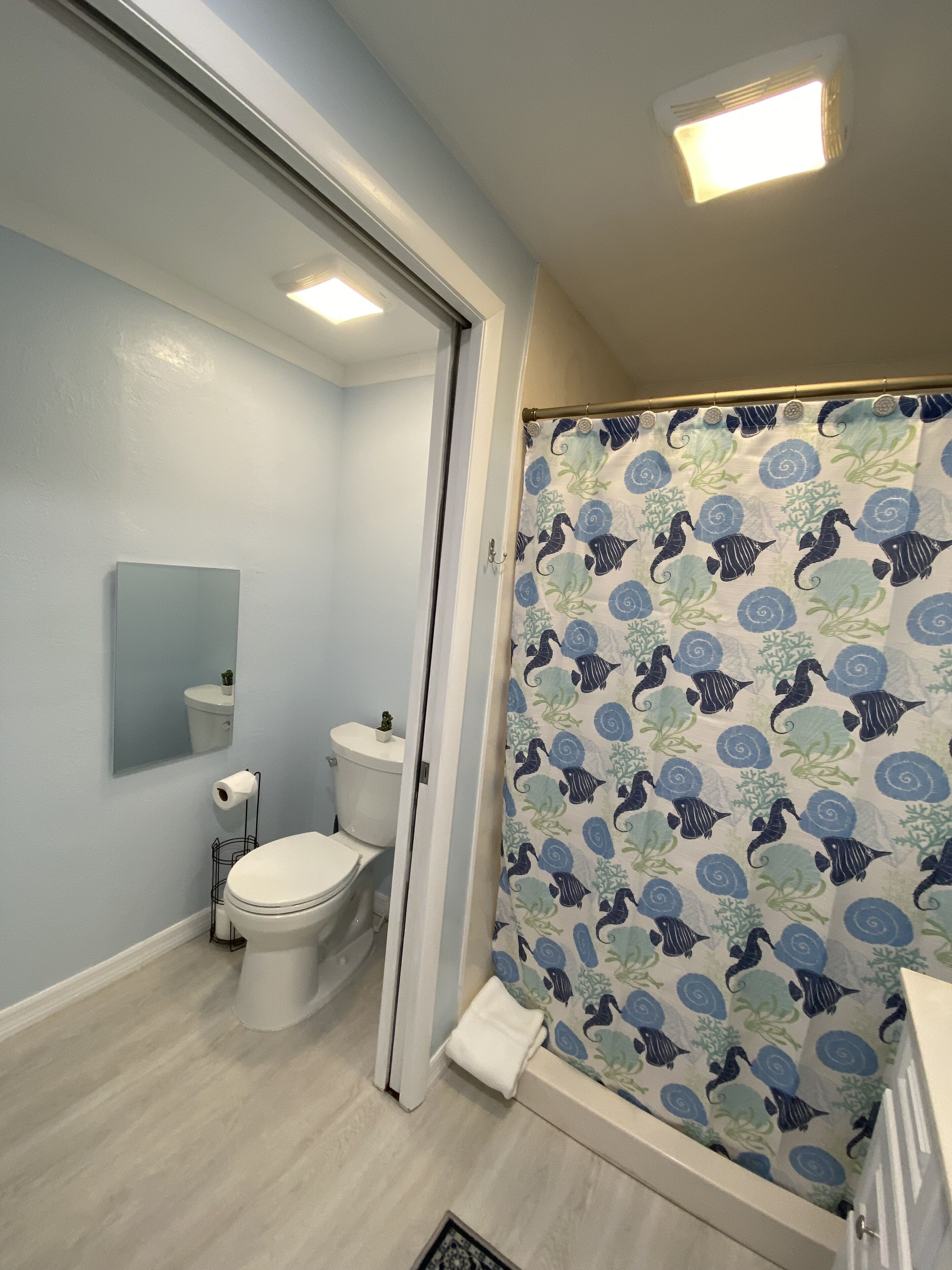 Un baño con inodoro, lavamanos, espejo y cortina de ducha con estampado azul y verde.