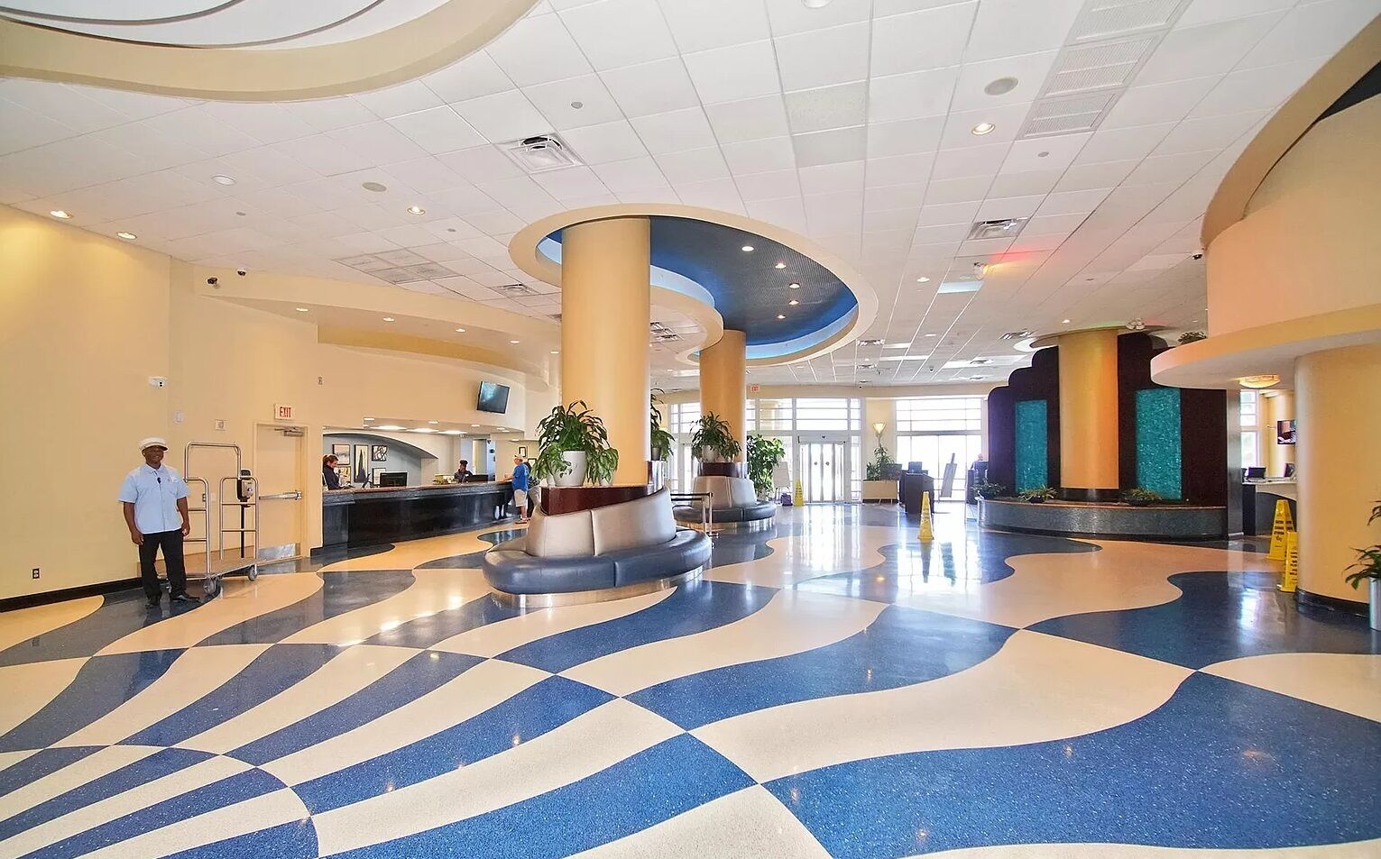 A spacious lobby with a check-in counter, a security desk, and a large central column with a plant.