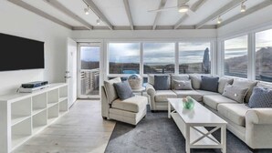 A spacious living room with a large TV, comfortable seating, and a balcony with a view. - Unit 511: Cottage | Ocean View | Nautilus (Amagansett)