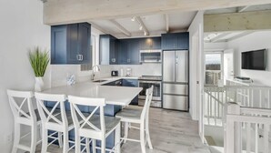 A modern kitchen with dark blue cabinets, stainless steel appliances, and a white dining area with a large island. - Unit 511: Cottage | Ocean View | Nautilus (Amagansett)