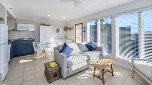 A modern living room with a sofa, a coffee table, and a dining area with a table and chairs. - Unit 611: Two-Bedroom | 1st Floor-Dune View | Periwinkle (Amagansett)