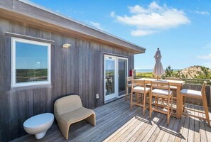 Eine Holzterrasse mit Tisch und Stühlen, einem Korbstuhl und einer Toilette.