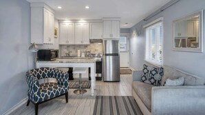 A modern kitchen with white cabinets, stainless steel appliances, a bar stool, and a grey sofa.