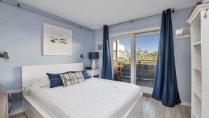 A bedroom with a large bed, a nightstand, a lamp, and a view of the outdoors through a sliding glass door.
