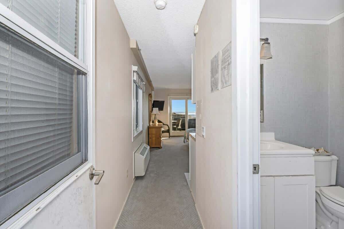 Un couloir étroit avec un radiateur, une commode en bois et une porte donnant sur une salle de bain équipée de toilettes et d’un lavabo.