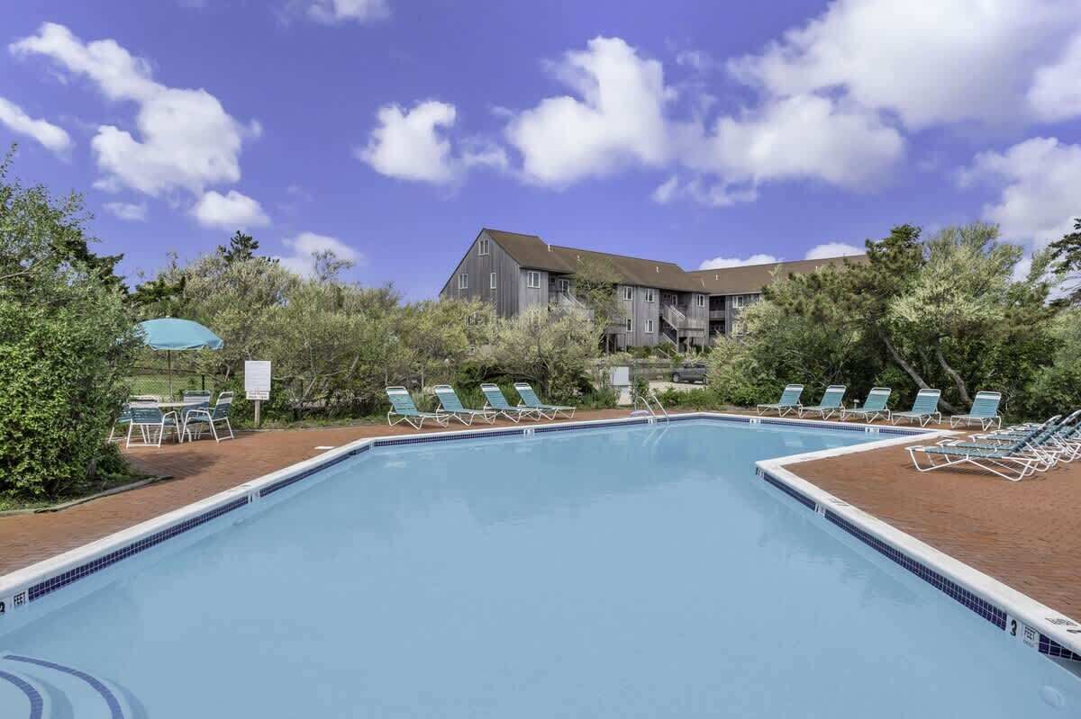 Una piscina con sillas de descanso y un edificio al fondo.