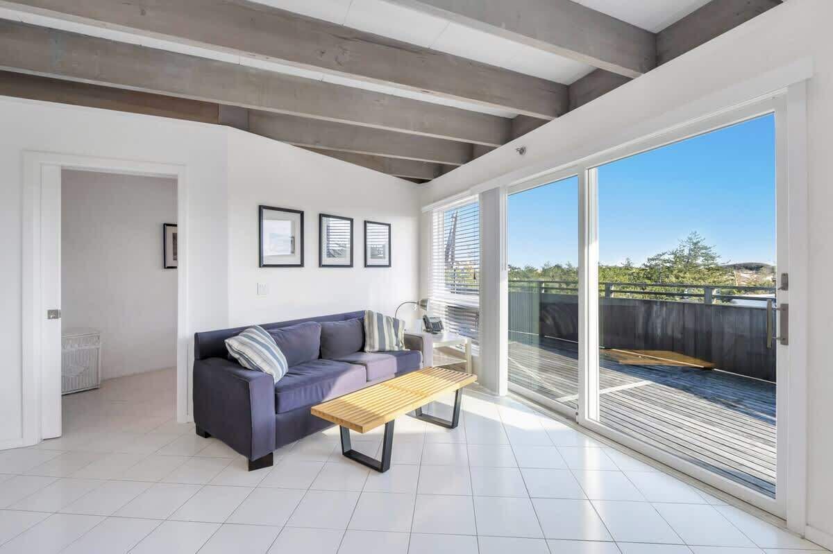 A modern living room with a sofa, a wooden table, and a large sliding glass door leading to an outdoor deck.