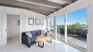 A modern living room with a sofa, a wooden table, and a large sliding glass door leading to an outdoor deck.