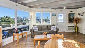 A spacious living area with a sofa, coffee table, and dining table. Large windows offer a view of the city.