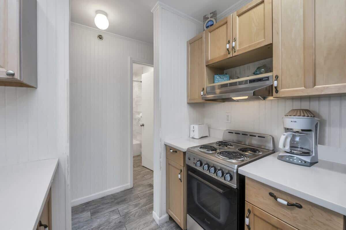 A compact kitchen with wooden cabinets, a gas stove, a coffee maker, and a toaster.
