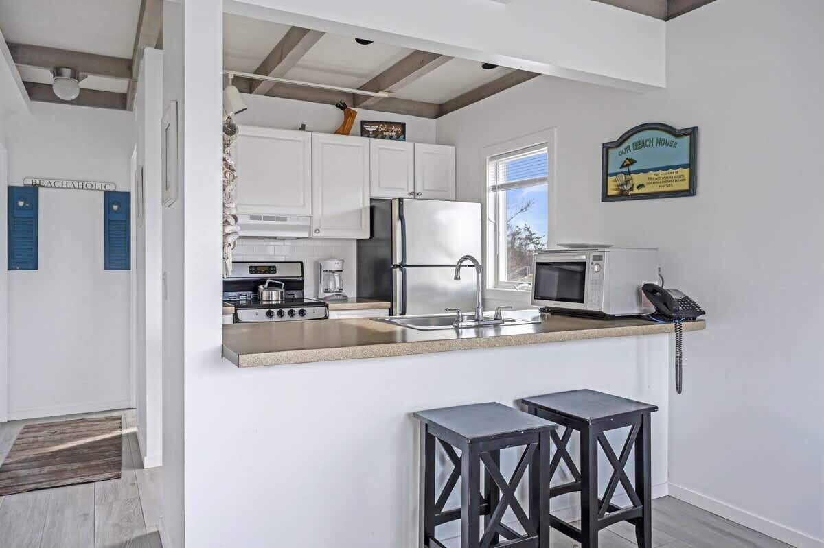 A modern kitchen with white cabinets, a stainless steel refrigerator, a microwave, and a coffee maker. There are two black stools at the counter.