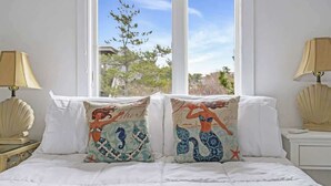 A bed with white bedding and two decorative pillows with mermaid designs.