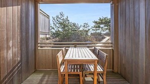 Una terraza de madera con una mesa y bancos, con vistas a un paisaje con árboles y un edificio.