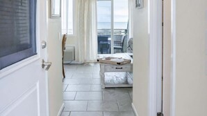 Un pasillo estrecho con una puerta a la izquierda, una ventana a la derecha y vistas a un balcón con una silla y una mesa.