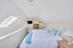 A bedroom with a skylight, a bed with white bedding and blue pillows, a wooden nightstand, and a dresser.
