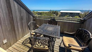 A wooden deck with a table and chairs, overlooking a beach and ocean. - Unit 1723: 1-Bedroom with Loft | 2nd Floor-Ocean Front Ocean View | Ocean Edge (Amagansett)
