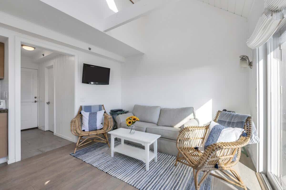 Un salon moderne comprenant un canapé, deux fauteuils en osier, une table basse et un téléviseur à écran plat fixé au mur.