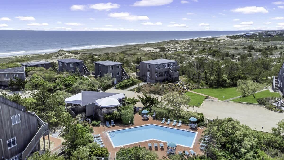 Un hotel frente a la playa con varias construcciones, una piscina y vistas al océano.