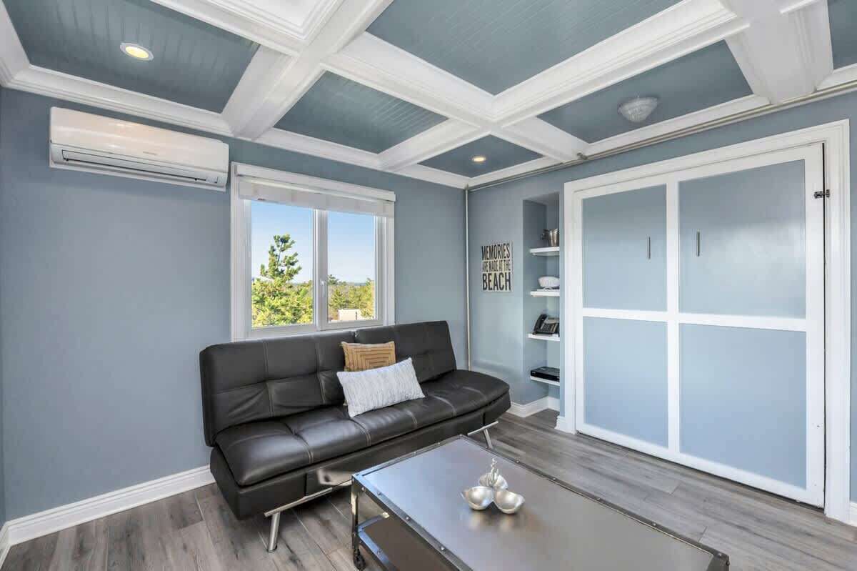 A modern living room with a black leather sofa, a coffee table, and a large window with a view of greenery.