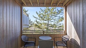 Een houten terras met een tafel en vier stoelen, met uitzicht op een boom en een hek.