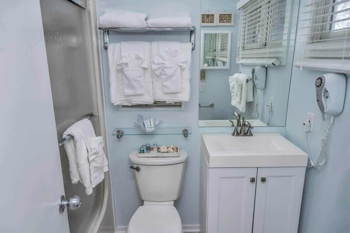 Une salle de bain comprenant des toilettes, une étagère en verre avec des articles de toilette, un lavabo avec un miroir et un téléphone.