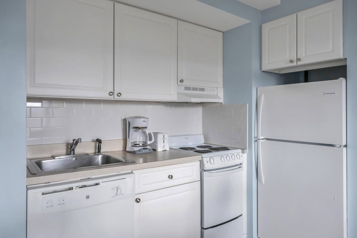 A kitchen with white cabinets, a stainless steel sink, a coffee maker, a stove, and a refrigerator.