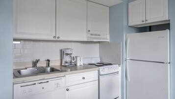 A kitchen with white cabinets, a stainless steel sink, a coffee maker, a stove, and a refrigerator.