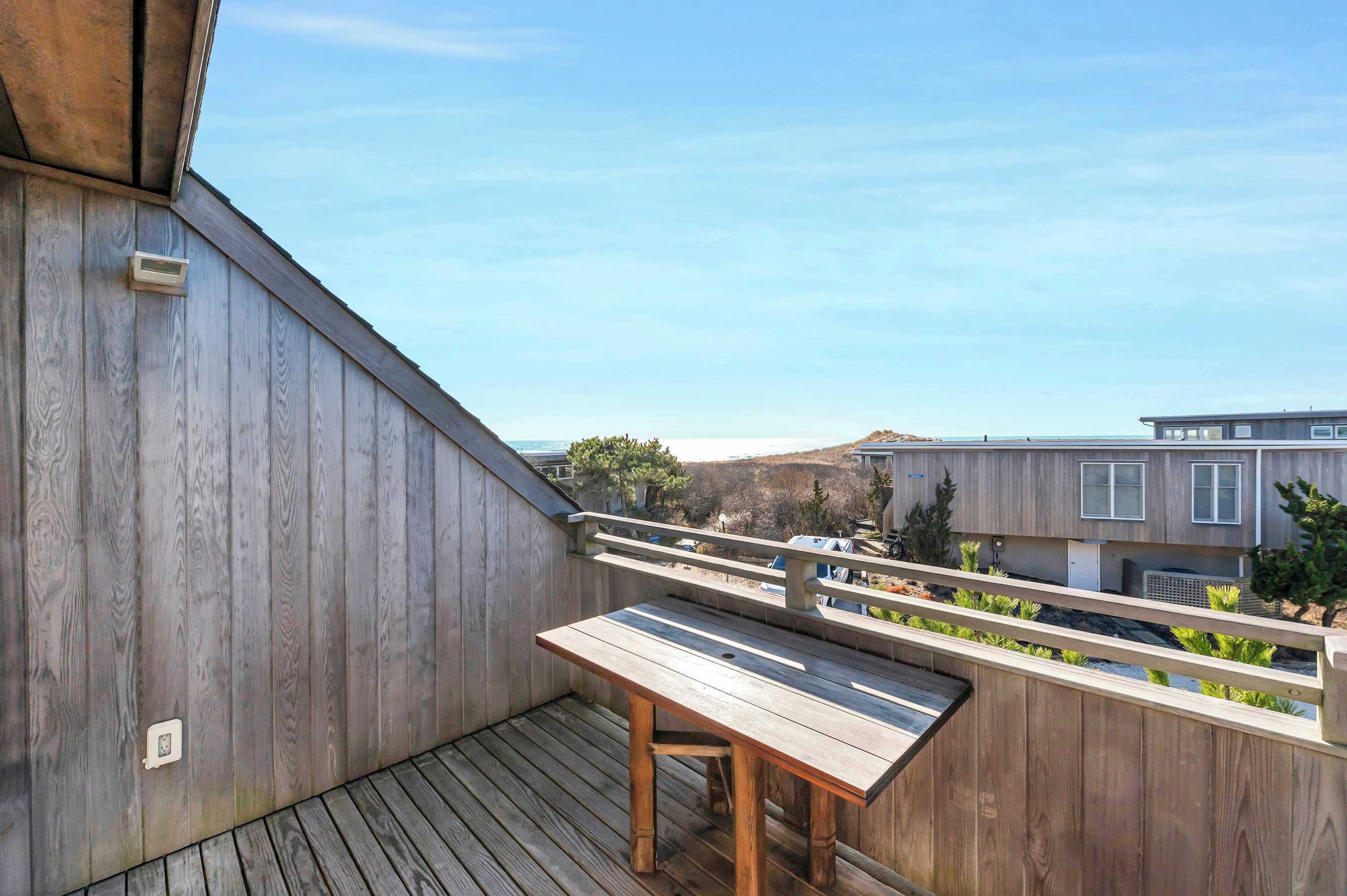 Eine Holzterrasse mit Tisch und Geländer, mit Blick auf eine Wohngegend mit Häusern und Bäumen.