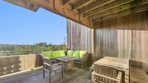 A wooden deck with a sofa and chairs, a table, and a view of the landscape.