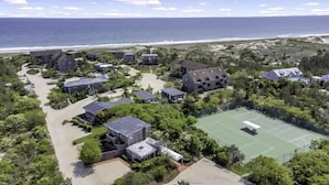 Vista aérea de una zona residencial costera con varias casas, una cancha de tenis y una playa al fondo.