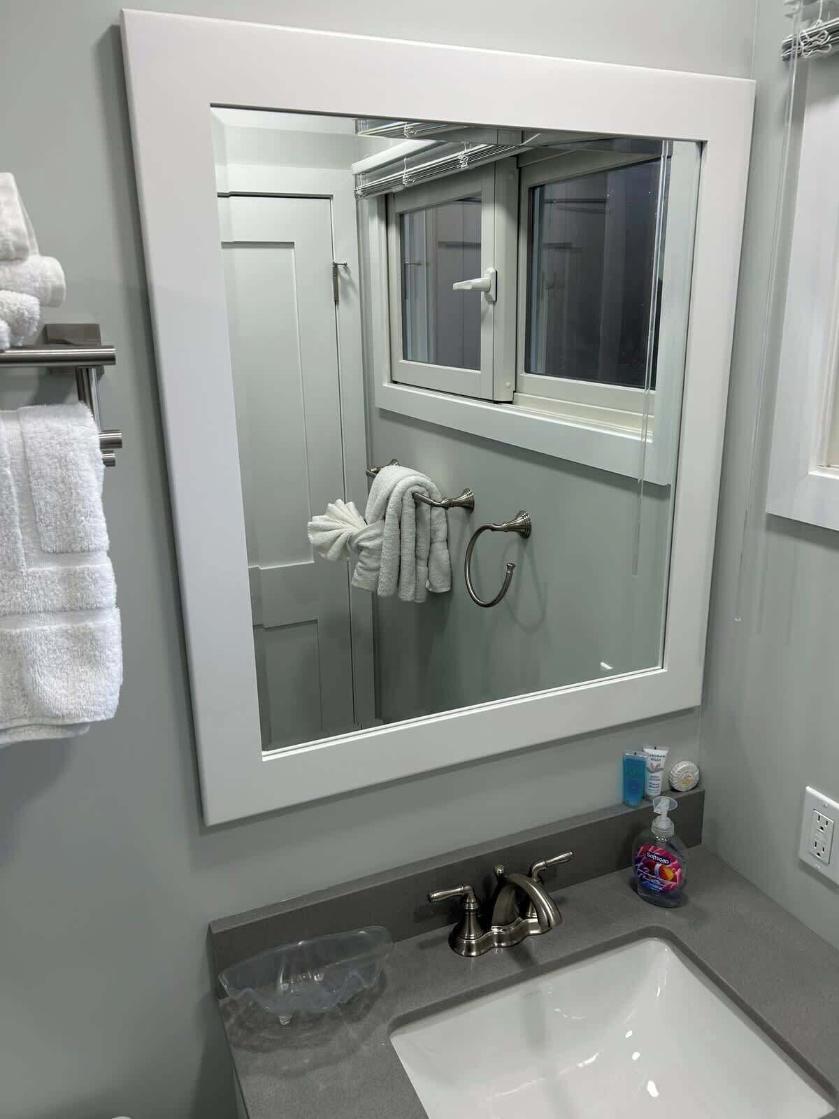 A bathroom with a large mirror, a sink, and a towel rack.