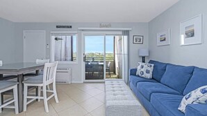 Una sala moderna con un sofá azul, una mesa de comedor con sillas y un balcón con vistas.