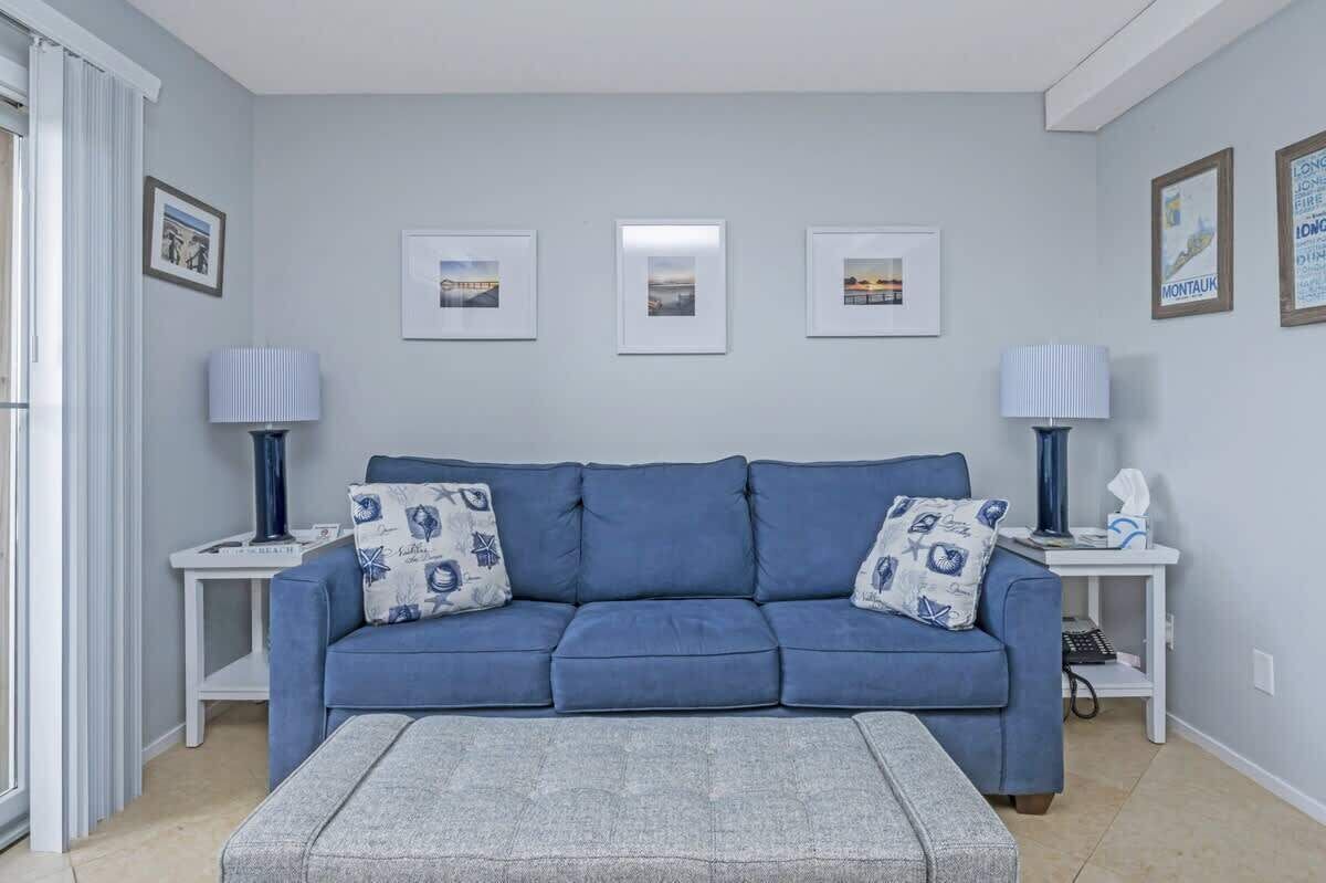 Un salon avec un canapé bleu, deux tables d’appoint avec des lampes et des tableaux encadrés accrochés au mur.