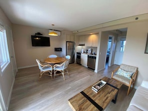 A modern kitchen with a dining table and chairs, a coffee maker, and a refrigerator.
