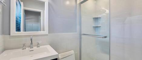 Un baño moderno con cabina de ducha de vidrio, un lavabo blanco y un inodoro.