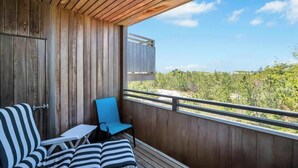 A balcony with a wooden floor, a striped sofa, a blue chair, and a small table. - Unit 1915: 1-Bedroom | 1st Floor-Dune View | Dunes West (Amagansett)
