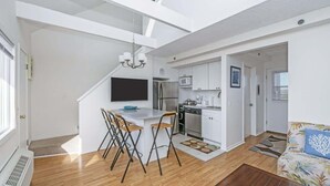 A modern apartment with a kitchen, dining area, and living room. It features a loft-style ceiling, a flat-screen TV, and a kitchenette.
