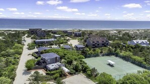 A coastal residential area with houses, a tennis court, and a beach in the background.