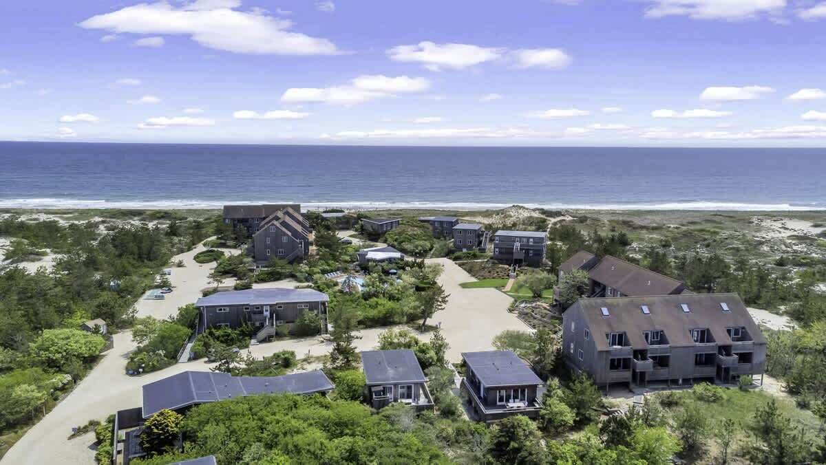 A coastal residential area with multiple houses, a clear view of the ocean, and a sandy beach.