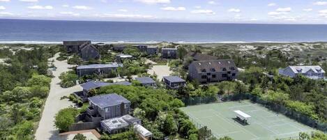 A coastal residential area with houses, a tennis court, and a beach in the background.