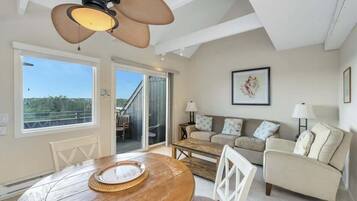 A spacious living room with a wooden dining table, a sofa set, and a ceiling fan.
