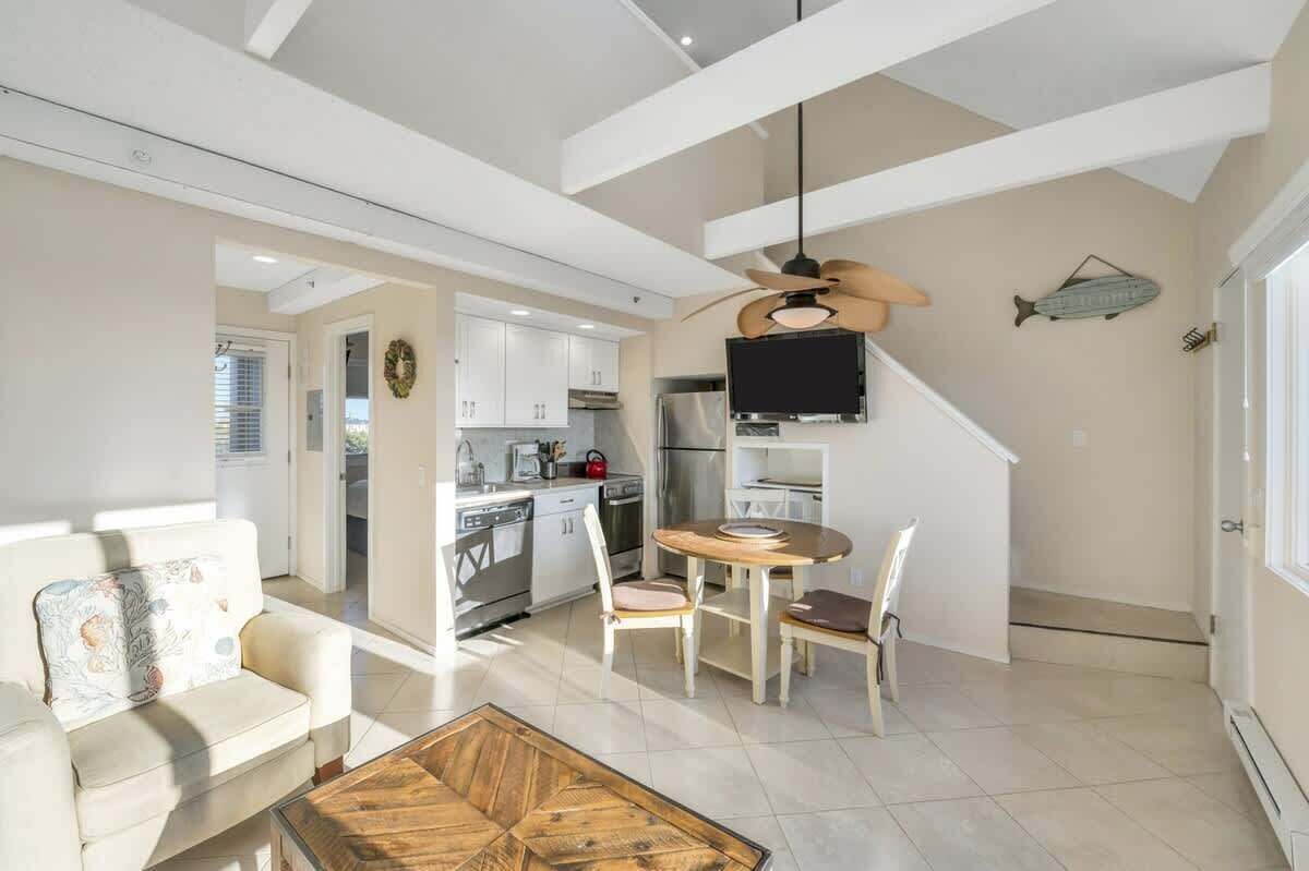 A modern kitchen with white cabinets, a dining area with a wooden table and chairs, and a ceiling fan.