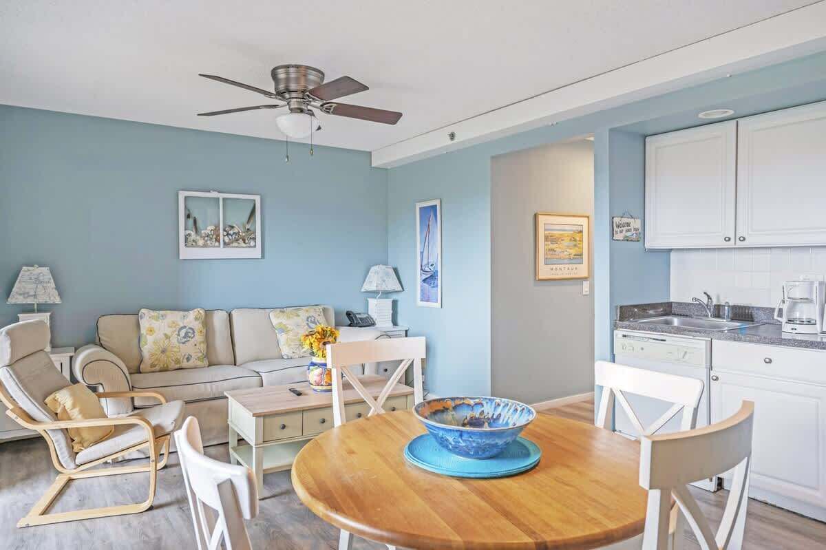 A living room with a sofa, chairs, a dining table, and a ceiling fan.