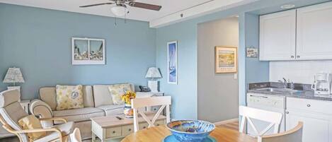 A living room with a sofa, chairs, a dining table, and a ceiling fan.