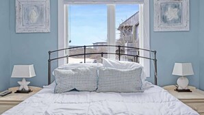 A bed with white bedding, two star-shaped nightstands, and a window with a view of buildings.